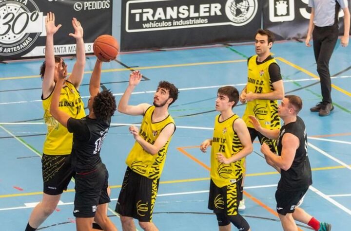 Basketball game in progress: players in yellow and black jerseys reach for the ball on an indoor court with banners in the background