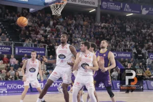 Basketball players contesting under the hoop as the ball flies toward the basket; crowded stands in the background.