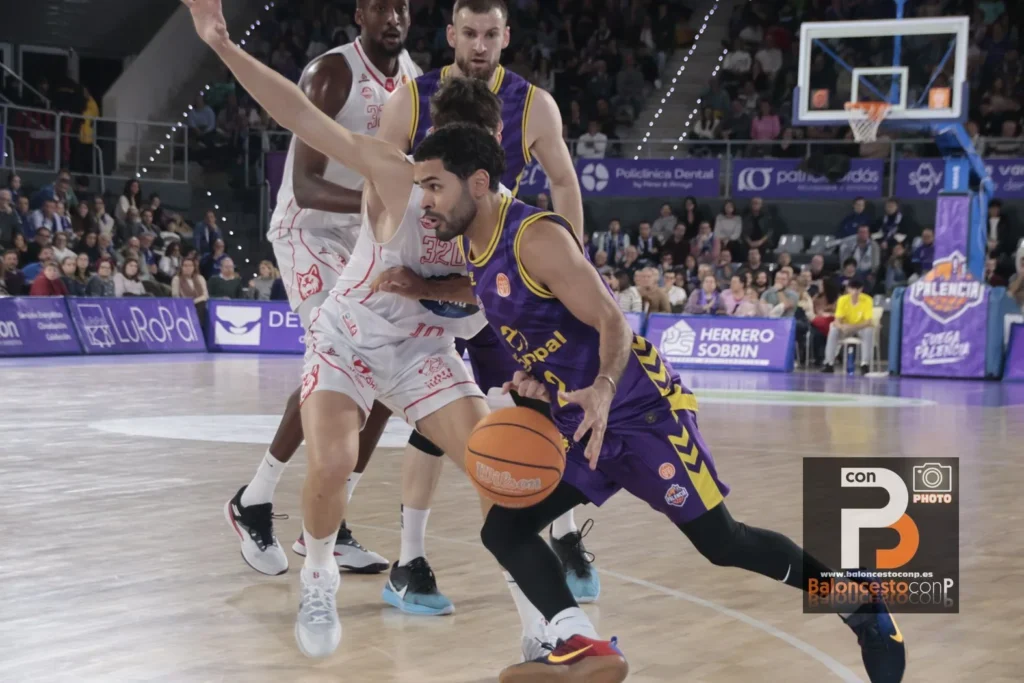 Basketball player in purple drives with the ball past a defender in white on a crowded court.