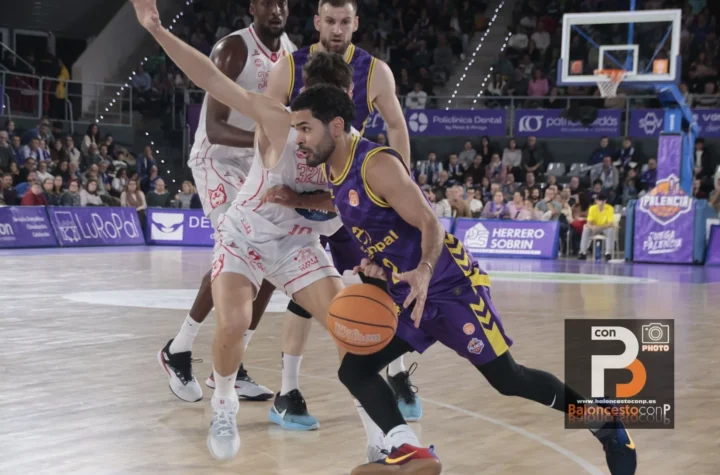 Basketball player in purple drives with the ball past a defender in white on a crowded court.