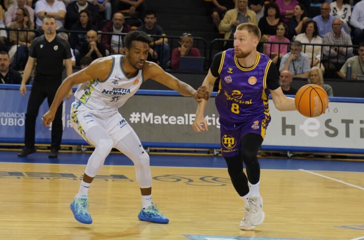 Purple-jerseyed guard (number 8) dribbles past a white-jersey defender as fans watch from the stands.