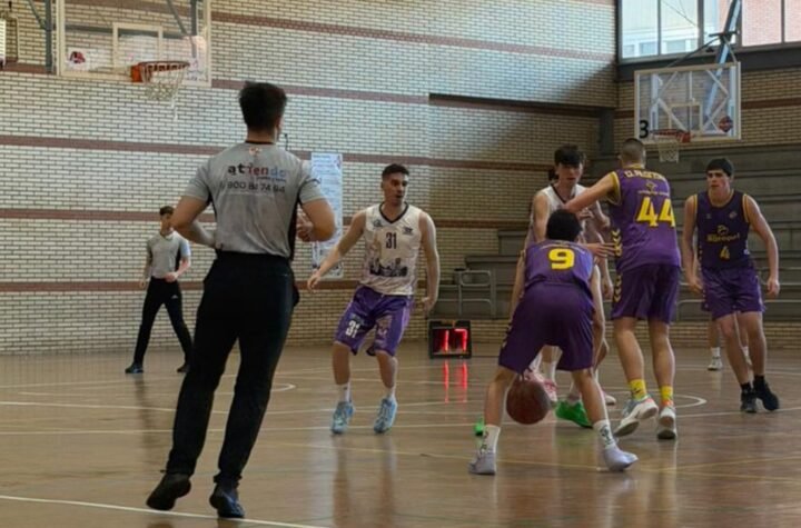 Indoor basketball game: players in purple and white uniforms contest the ball near the key while a referee watches from the foreground.