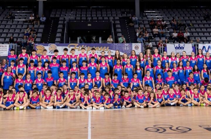 Large group of children and adults in colorful basketball uniforms posing for a team photo on an indoor court.