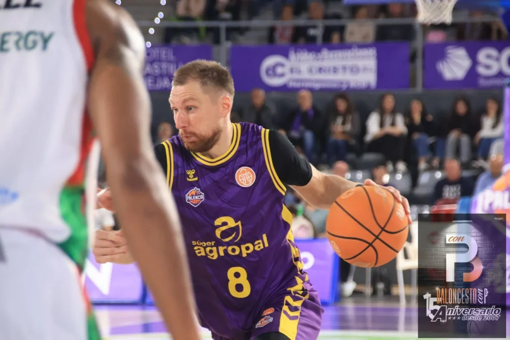 Basketball player in a purple uniform with number 8 dribbling the ball toward the basket, with spectators in the background.