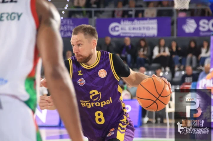 Basketball player in a purple uniform with number 8 dribbling the ball toward the basket, with spectators in the background.