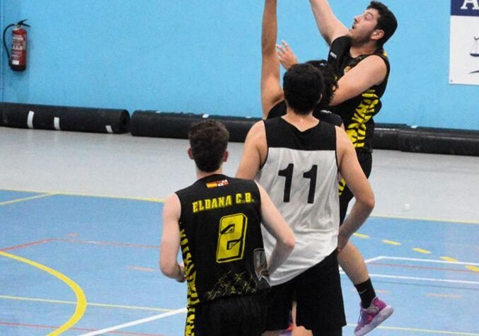 Basketball game in progress: a player in a black-yellow jersey soars for a shot near the hoop while two defenders reach up nearby.