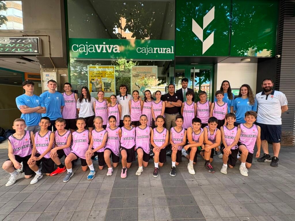 Group of young basketball players in pink uniforms posing with coaches outside a bank storefront.