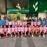 Group of young basketball players in pink uniforms posing with coaches outside a bank storefront.