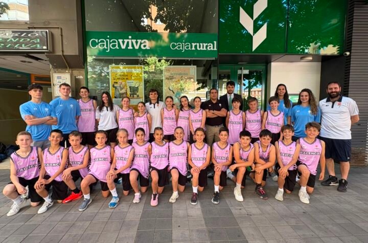 Group of young basketball players in pink uniforms posing with coaches outside a bank storefront.