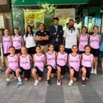 Group of young basketball players in pink Palencia jerseys with coaches, posing outdoors in front of a storefront.
