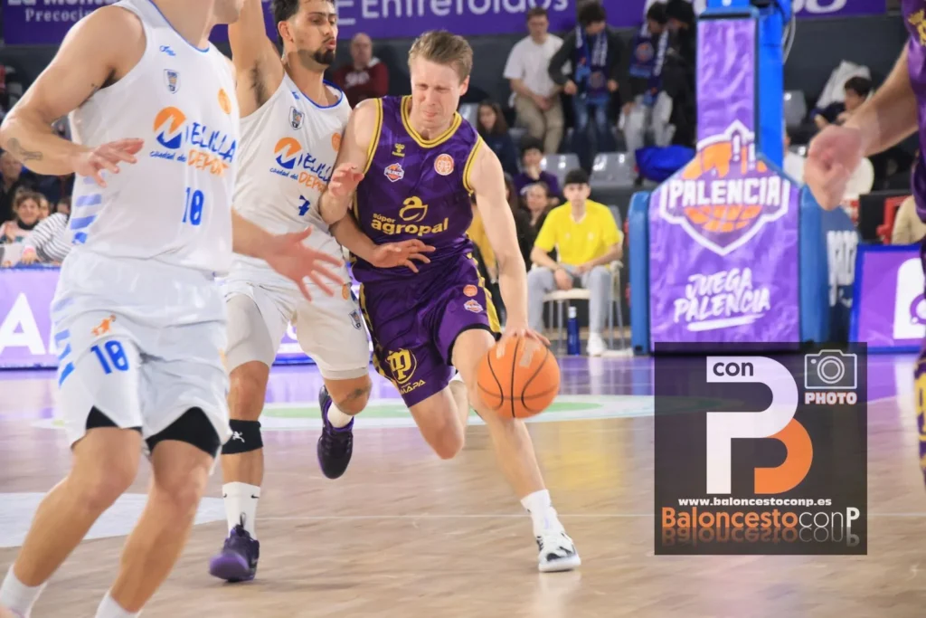 Basketball player in a purple uniform dribbles past white-uniform defenders during a fast break on a polished court with spectators in the background.