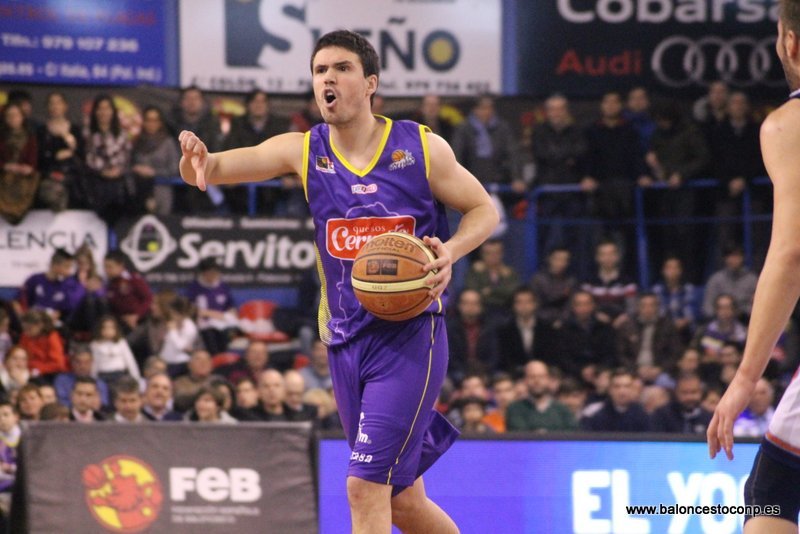 Basketball player in purple jersey shouts while dribbling the ball on court, with a packed crowd in the background.