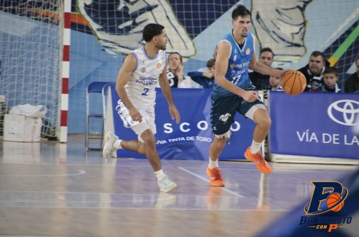 Basketball players in white and blue jerseys chase the ball on an indoor court, with orange shoes and a blue advertising banner in the background.