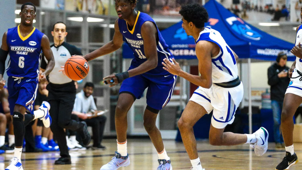 Basketball game in progress with players in blue and white uniforms chasing the ball on a court.