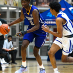 Basketball game in progress with players in blue and white uniforms chasing the ball on a court.