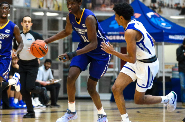 Basketball game in progress with players in blue and white uniforms chasing the ball on a court.