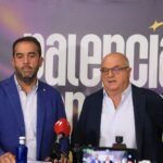 Two men in suits stand at a press conference with microphones; backdrop reads 'baloncesto' in large letters.