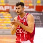 Basketball player in a red jersey claps his hands on a court, focused during a game warm-up.