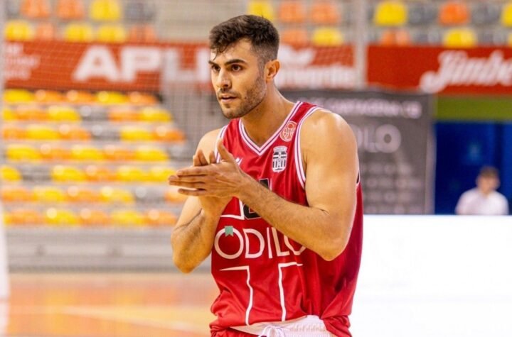 Basketball player in a red jersey claps his hands on a court, focused during a game warm-up.