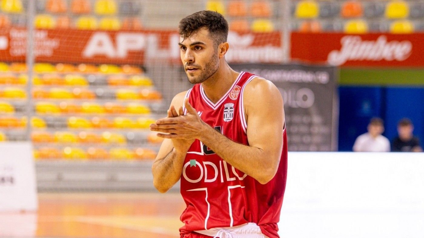 Basketball player in a red jersey claps his hands on a court, focused during a game warm-up.